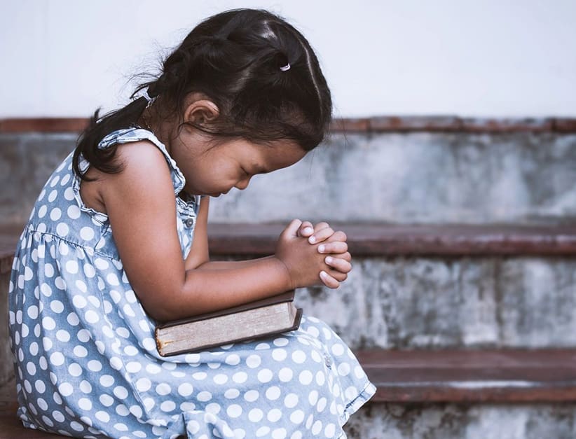 A little girl sitting on the steps holding her hands in prayer.