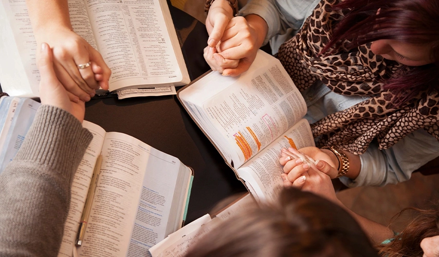 A group of people holding hands around a bible.