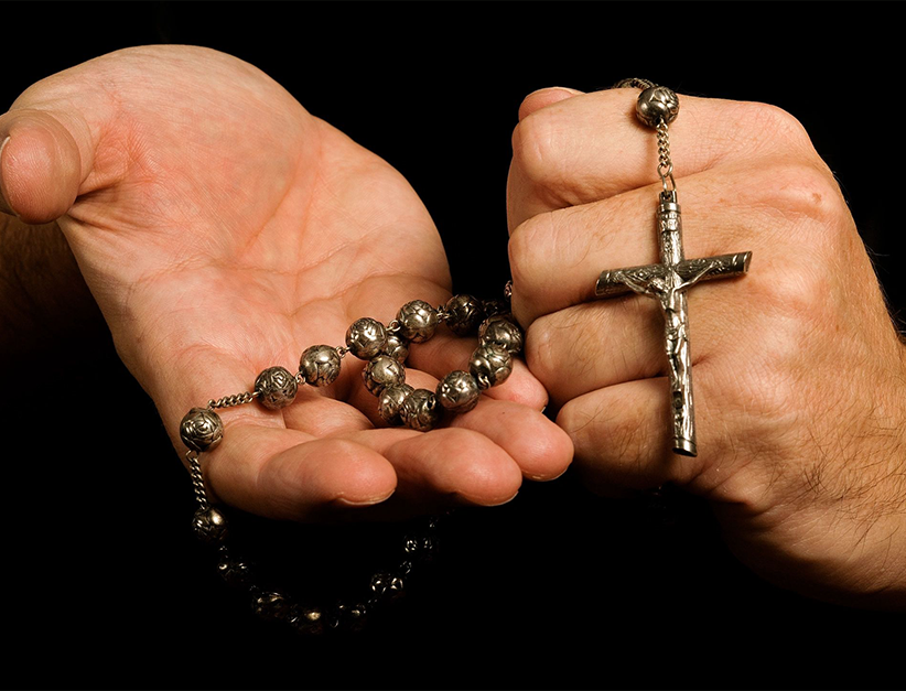 A man's hands holding a rosary and a cross.